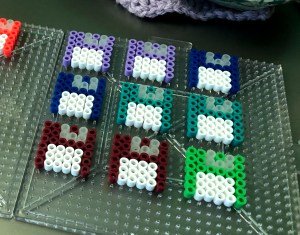 Brightly colored perler bead crafts arranged in the shape of floppy disks.