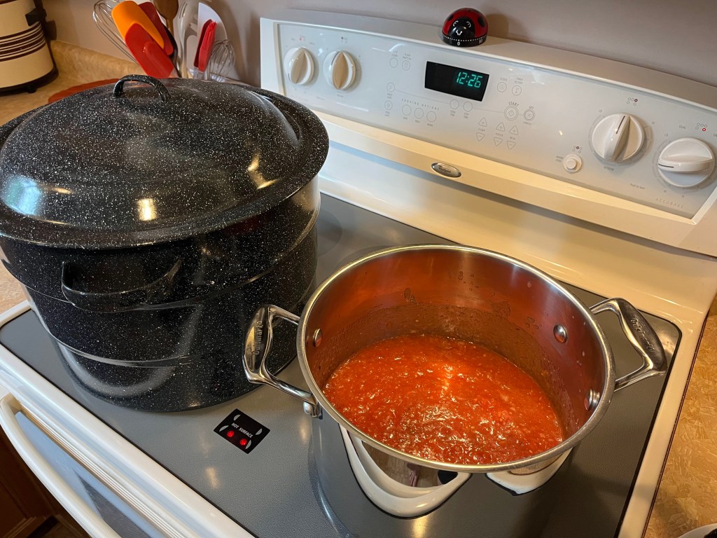 Two giant pots on the stove, one full of pizza sauce