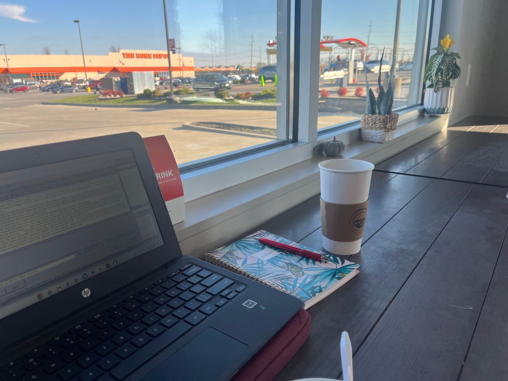 A laptop and coffee in front of a window facing a home depot