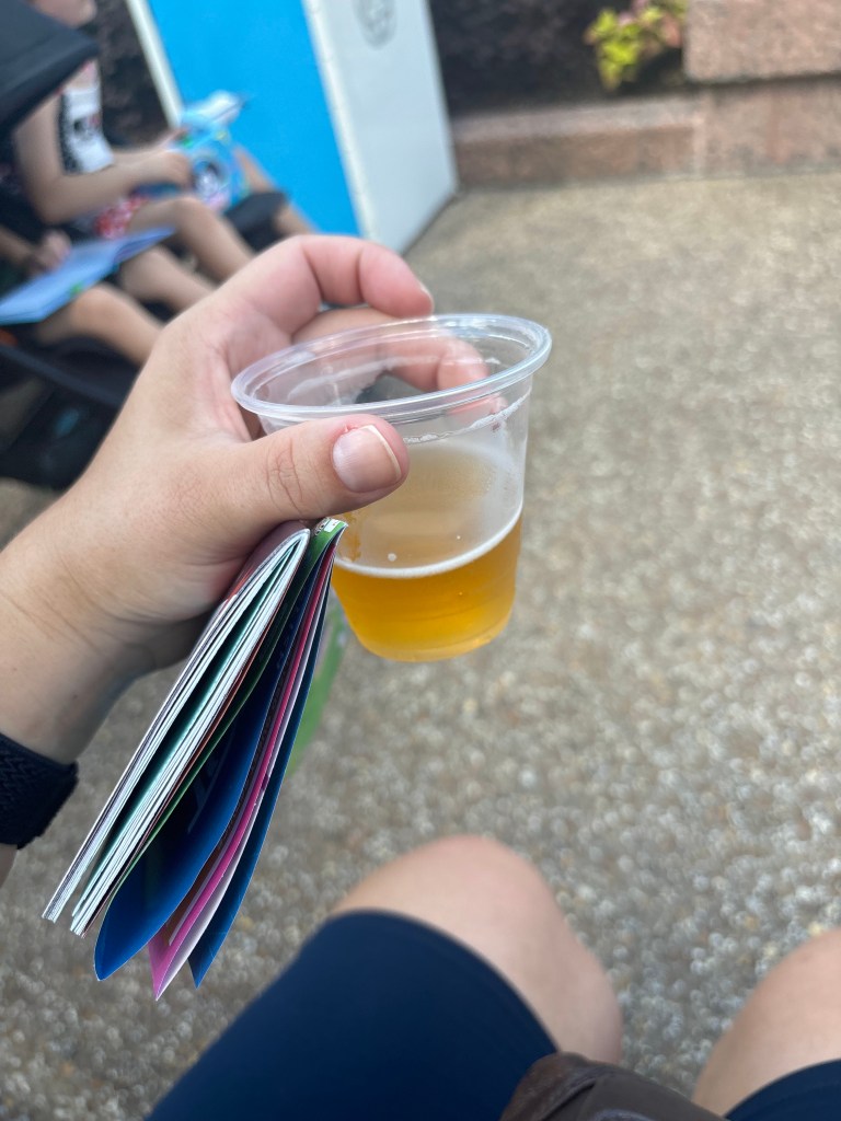The author's hand holding a small cup of beer.