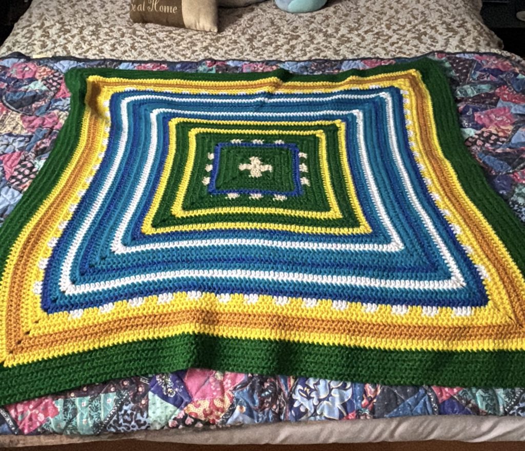 A colorful crochet temperature square laid out on a bed.