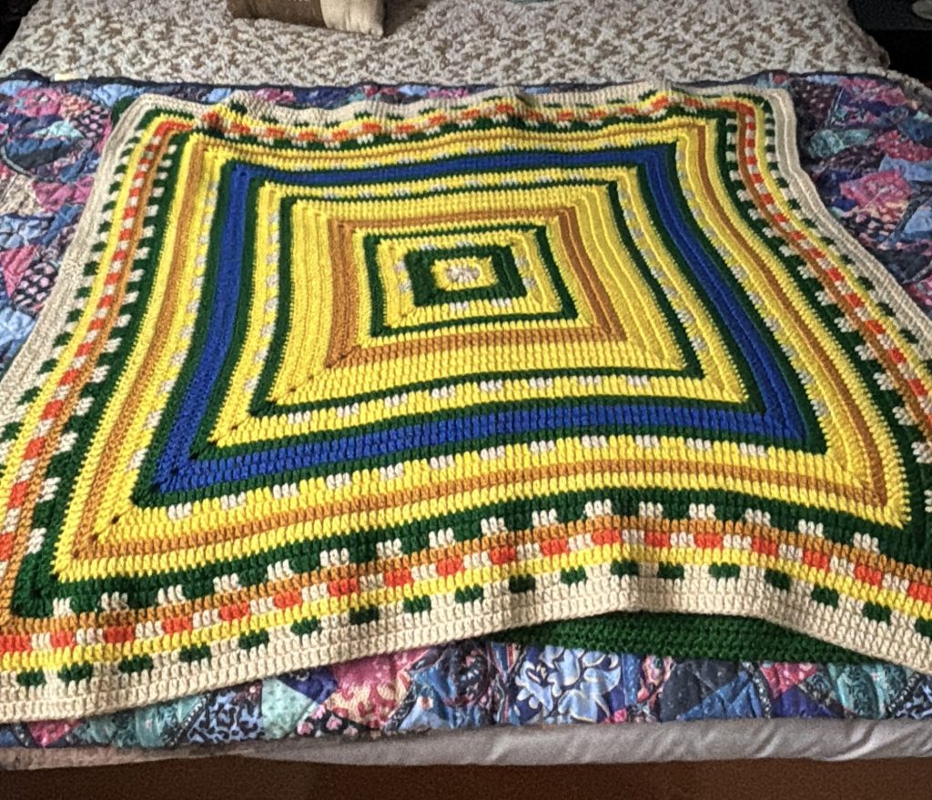 A colorful crochet temperature square laid out on a bed.