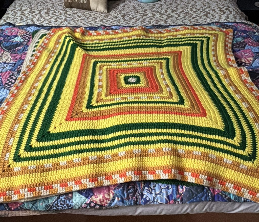 A colorful crochet temperature square laid out on a bed.