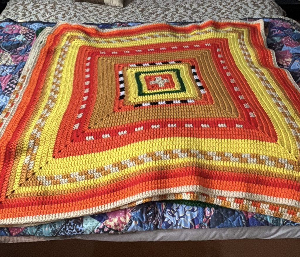 A colorful crochet temperature square laid out on a bed.