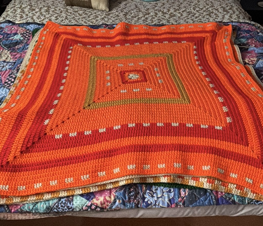 A colorful crochet temperature square laid out on a bed.