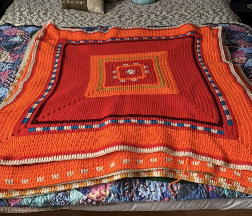 A colorful crochet temperature square laid out on a bed.
