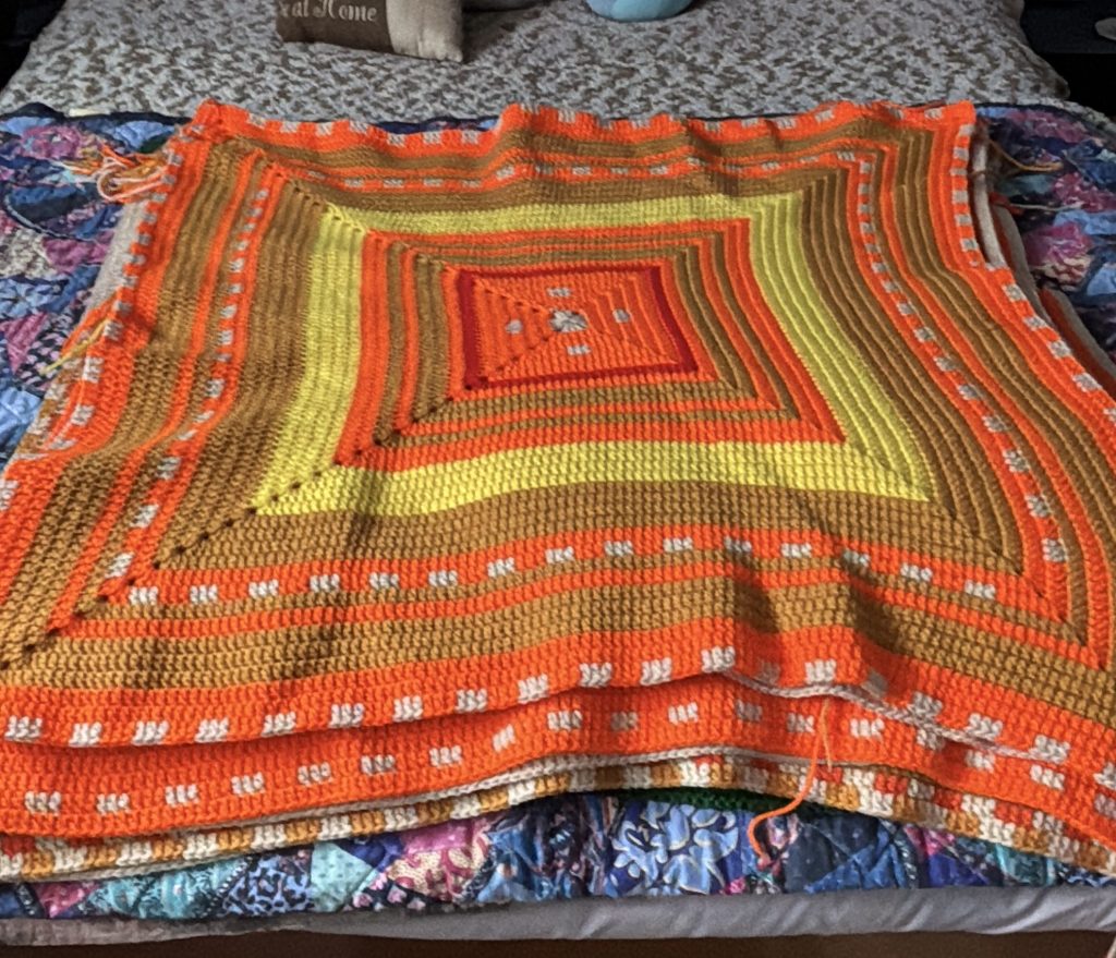 A colorful crochet temperature square laid out on a bed.