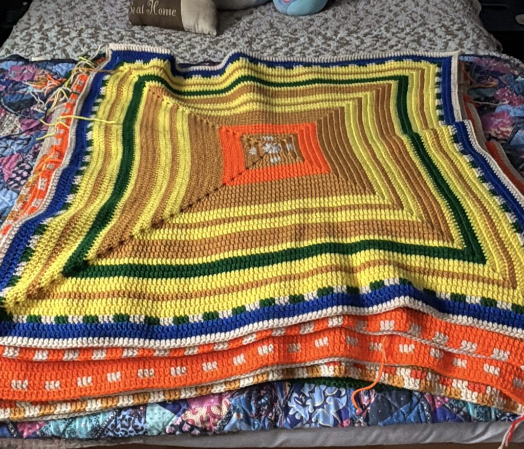 A colorful crochet temperature square laid out on a bed.