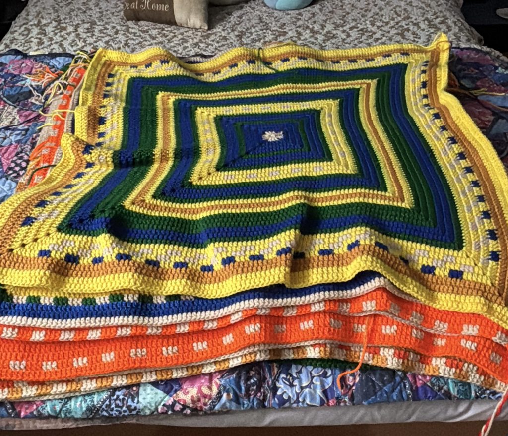 A colorful crochet temperature square laid out on a bed.
