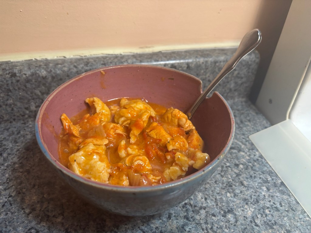 A bowl of Hungarian Goulash, a reddish soup with dumplings and chicken