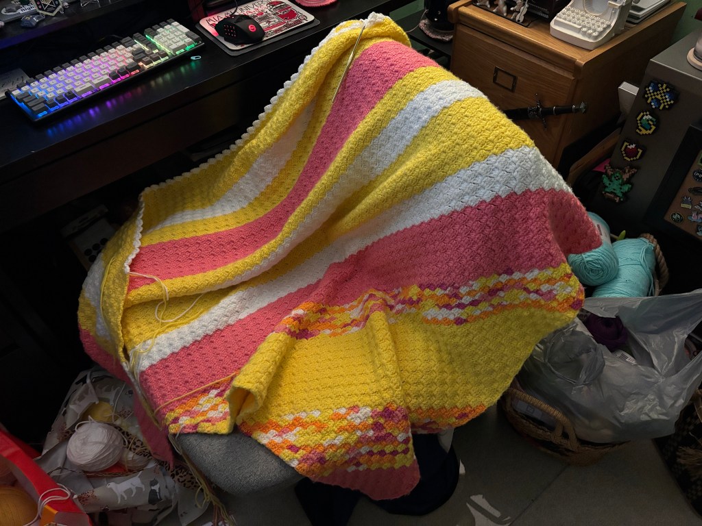 a crochet blanket in progress draped over a computer desk chair
