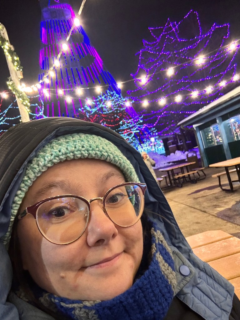 the author, bundled up in a winter coat and scarf and hat, in front of a winter lights display at Kings Island